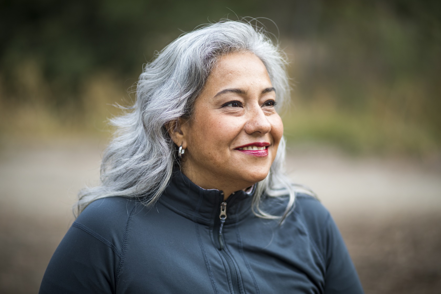 Smiling elderly woman, looking into the distance, outdoors.